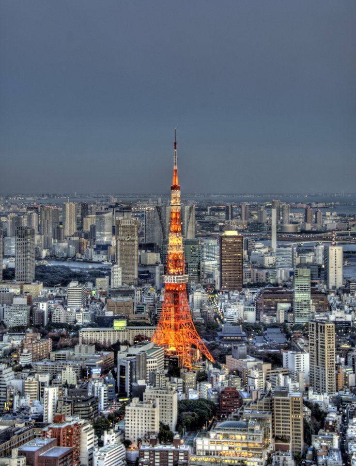 Tokyo Tower lit orange among the city buildings at dusk, seen from high above