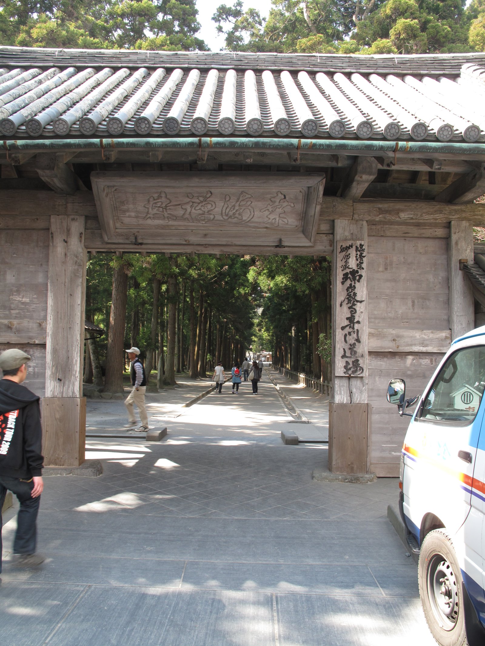 A wooden temple gate at the start of a tree-lined path