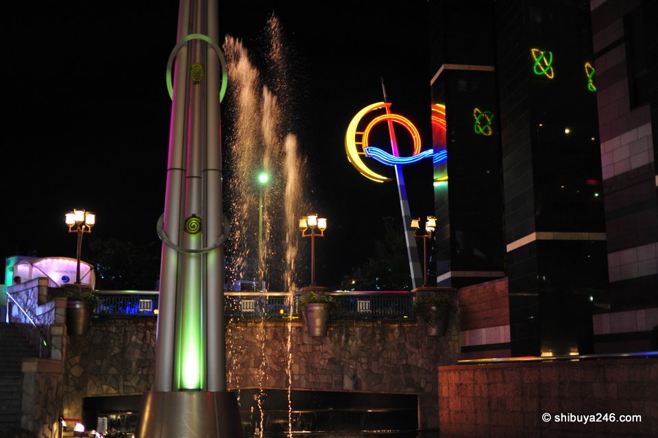 A tall fountain tower beside a lit-up logo