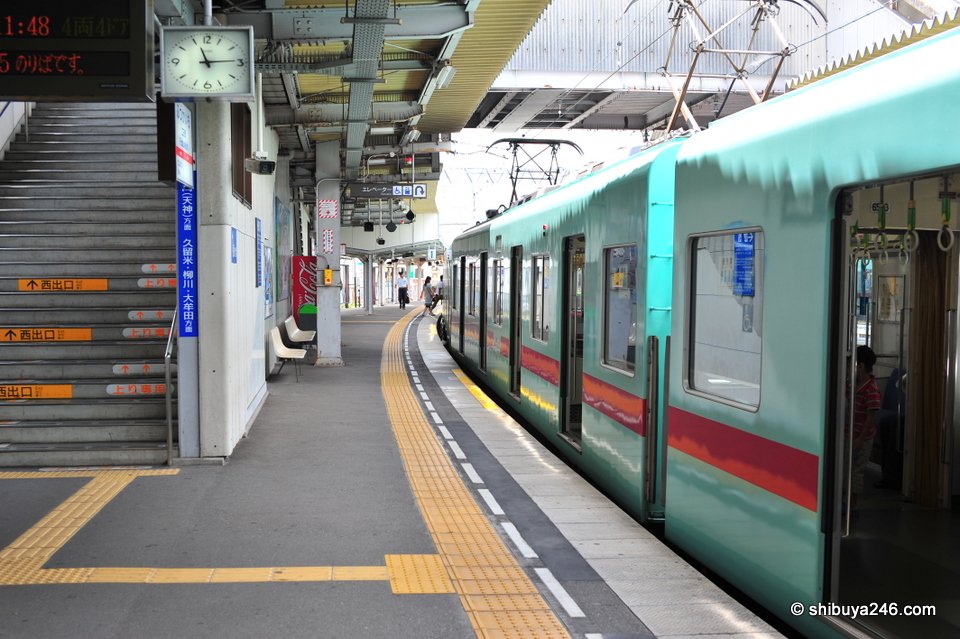 A green Nishitetsu train at a station platform