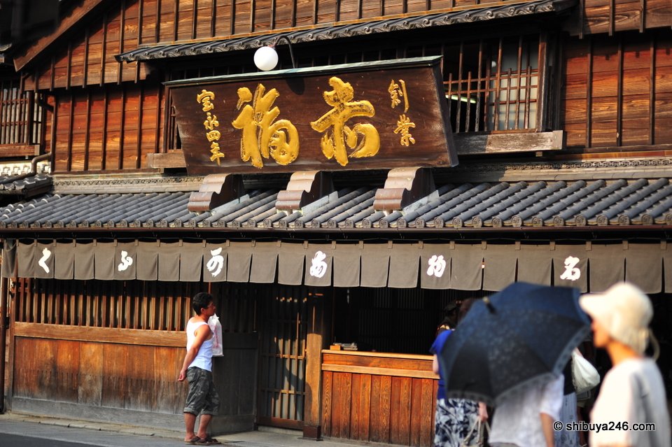 A large wooden shop building with a gold signboard
