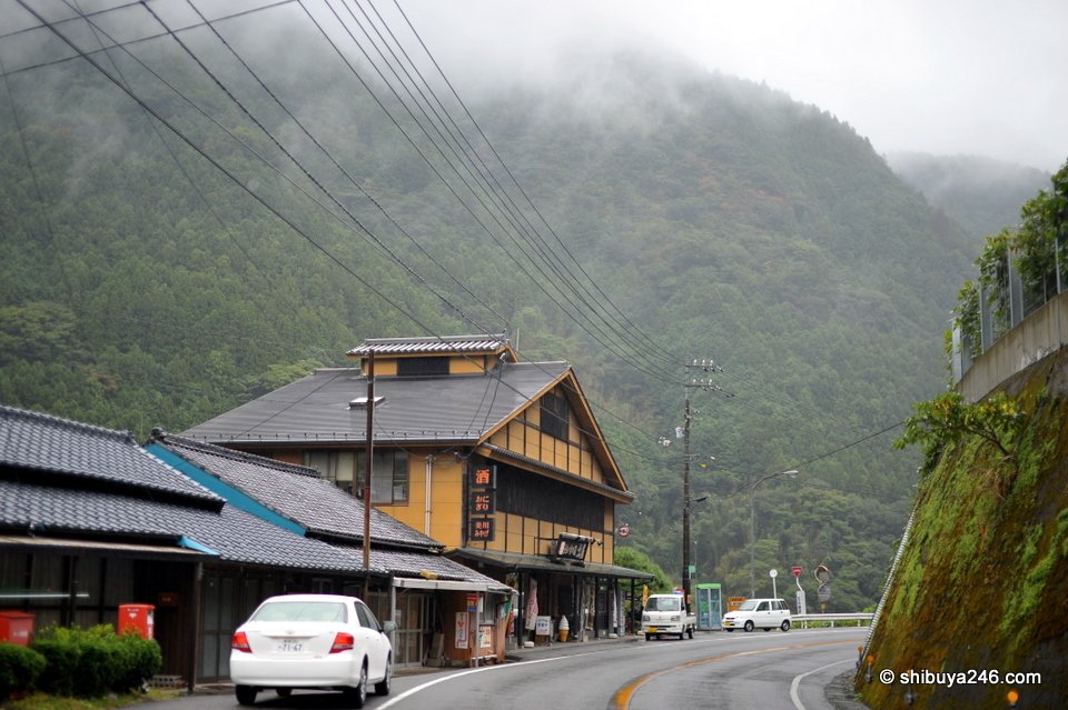 A large old wooden building beside the road with misty hills behind