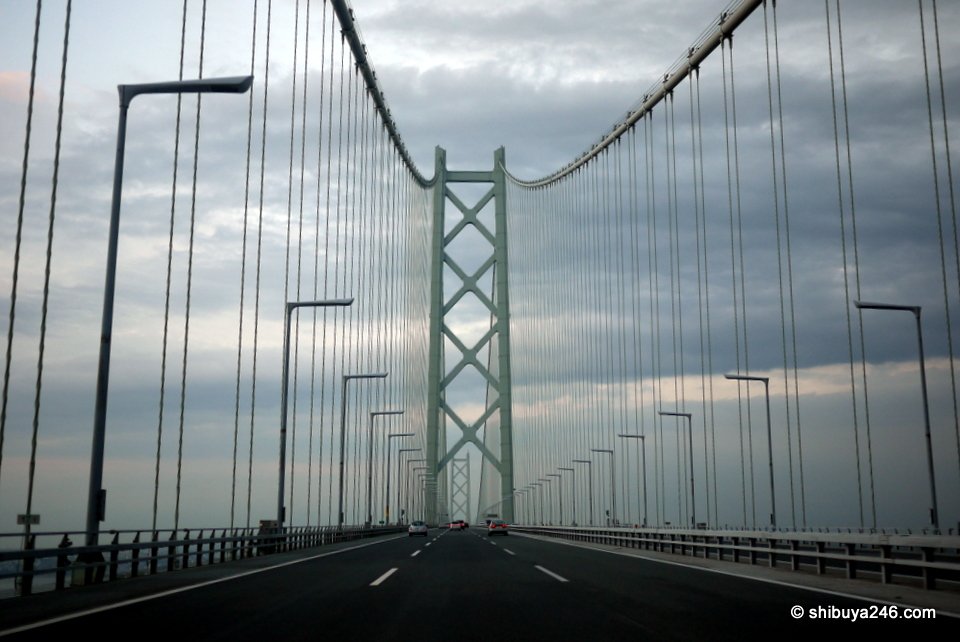 Looking up at a green bridge tower and its main cables from the road