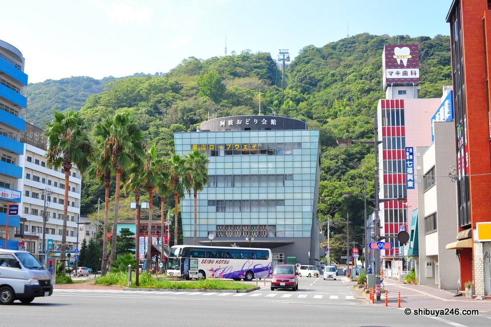 A city street with palm trees and green hills behind