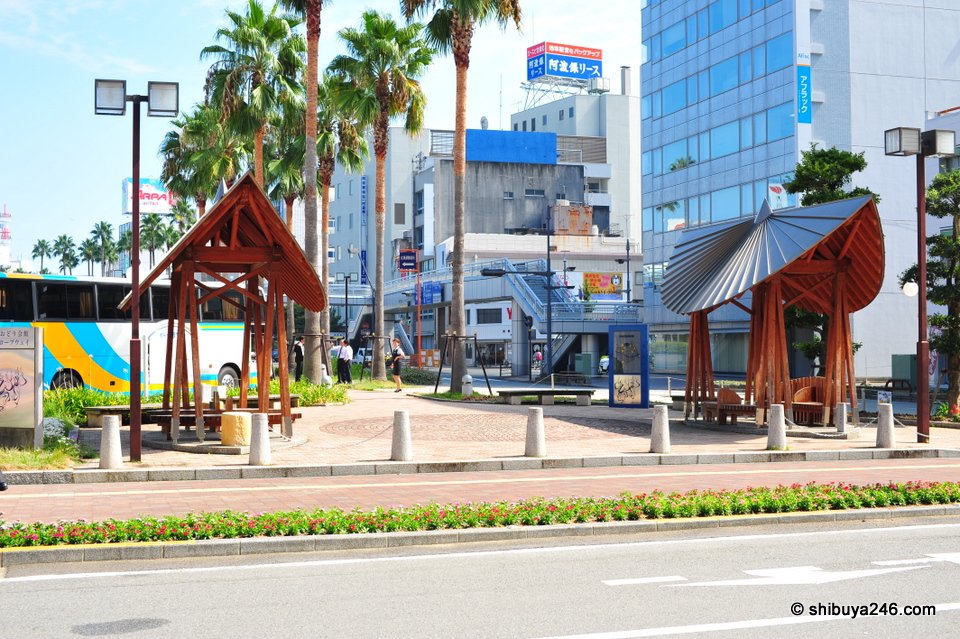 A plaza with palm trees and wooden shelters
