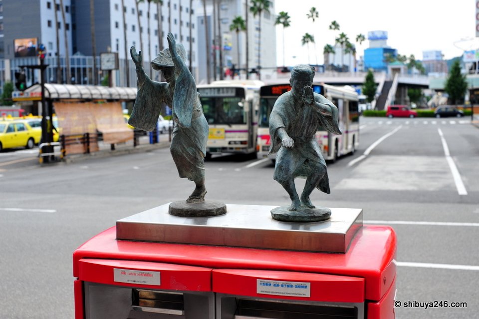 Bronze statues of Awa Odori dancers on top of a red postbox