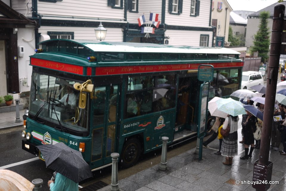 A green retro-style tourist bus on a narrow street