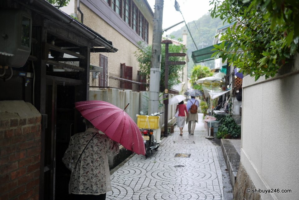 A narrow lane with a person carrying a pink umbrella
