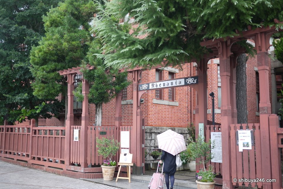A red-brick building behind a wooden fence with visitors under umbrellas