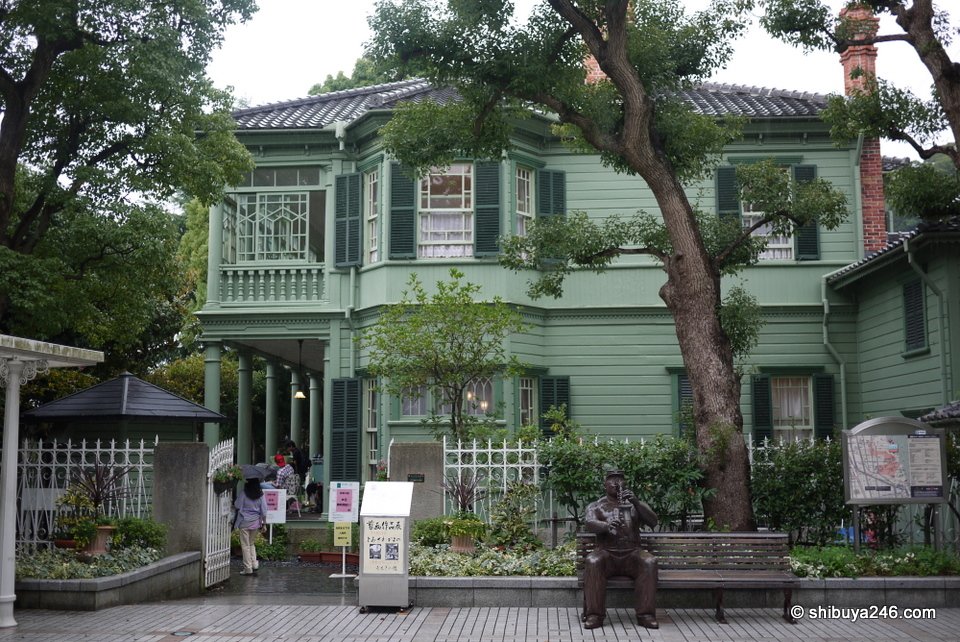 A pale green wooden Western-style house among trees