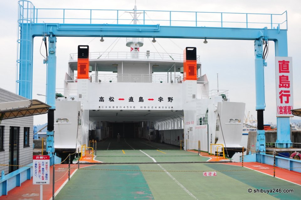A car ferry with its ramp down at a port, with a sign reading 直島行