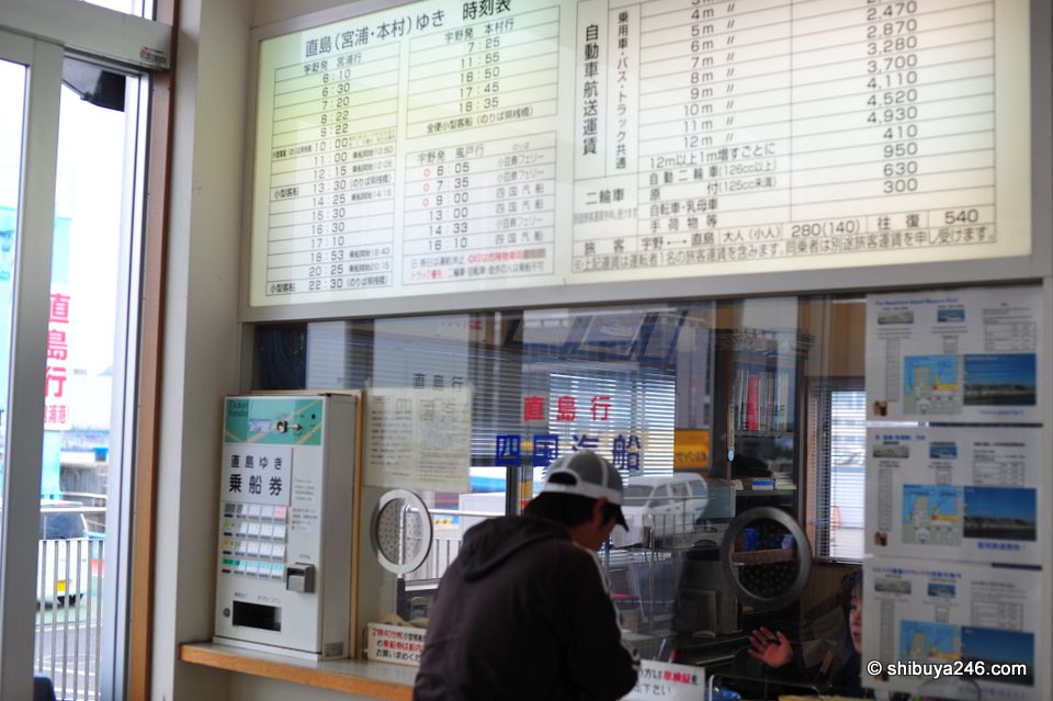 A man buying tickets at a ferry ticket window under a timetable