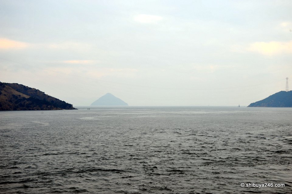 A pointed island on the horizon between two headlands