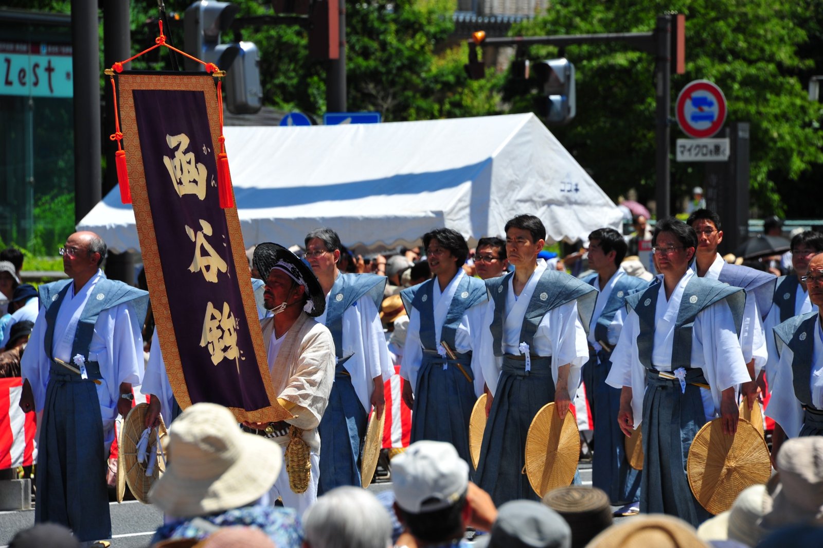Men in blue kimono walking with a banner