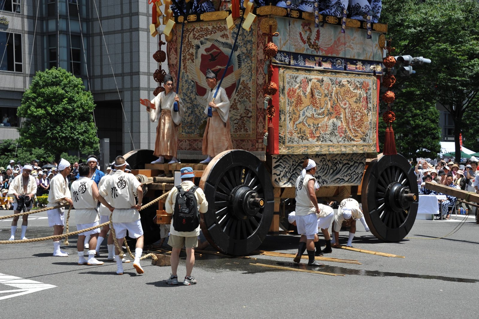 A float with large wooden wheels and pullers in front