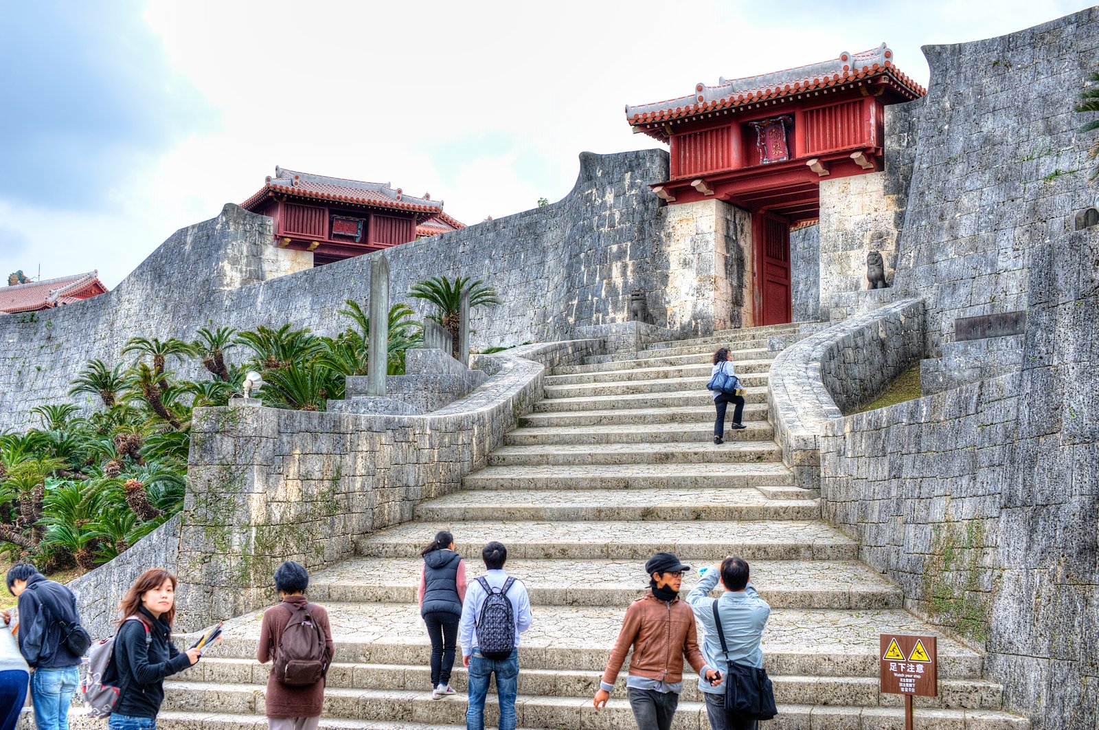 Visitors climbing stone steps below curved stone walls and a red gate