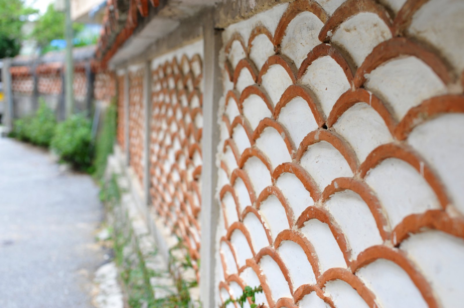 A wall made of curved red roof tiles beside a lane