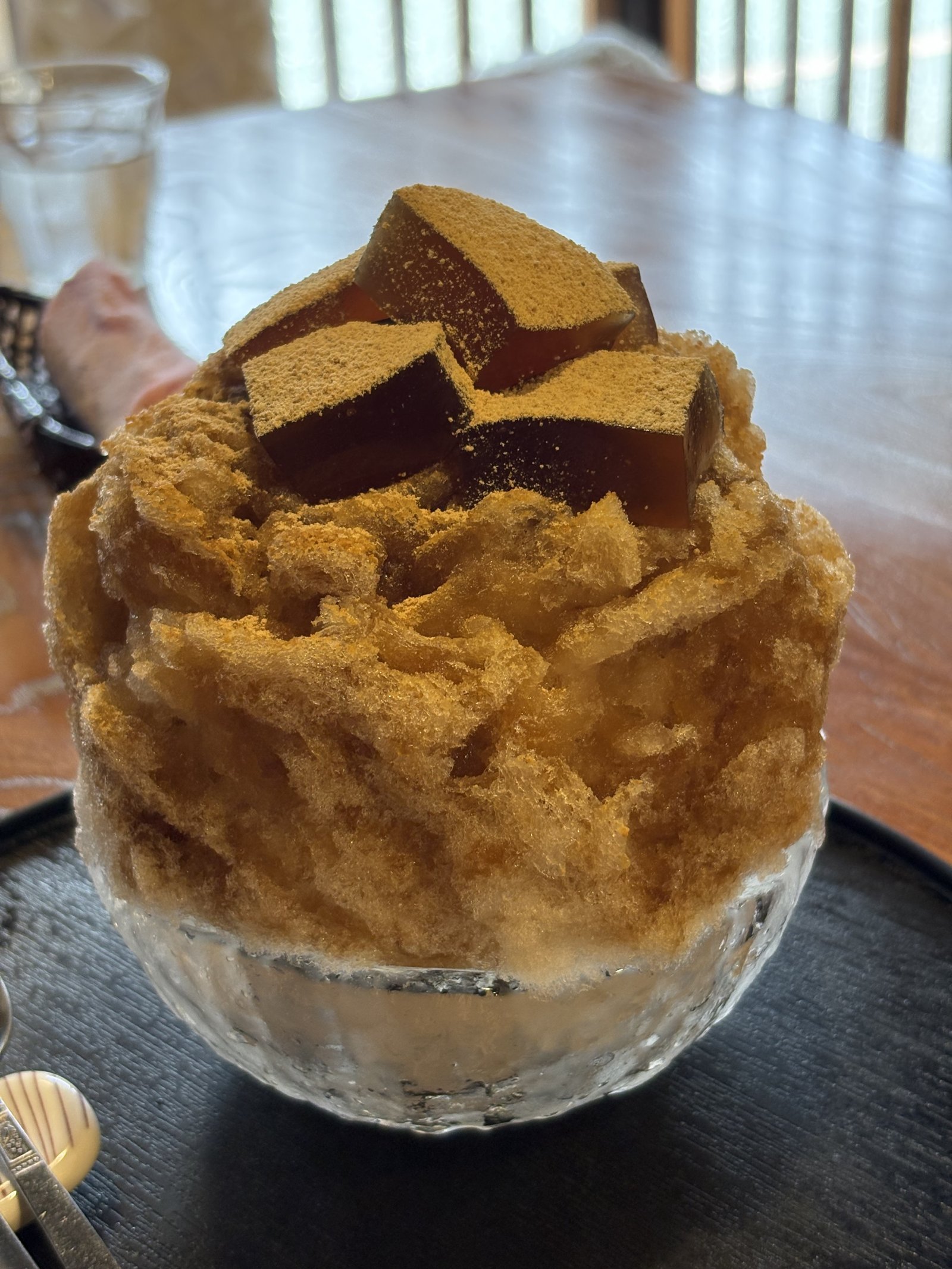 A bowl of shaved ice with a brown syrup and cubes of jelly on top
