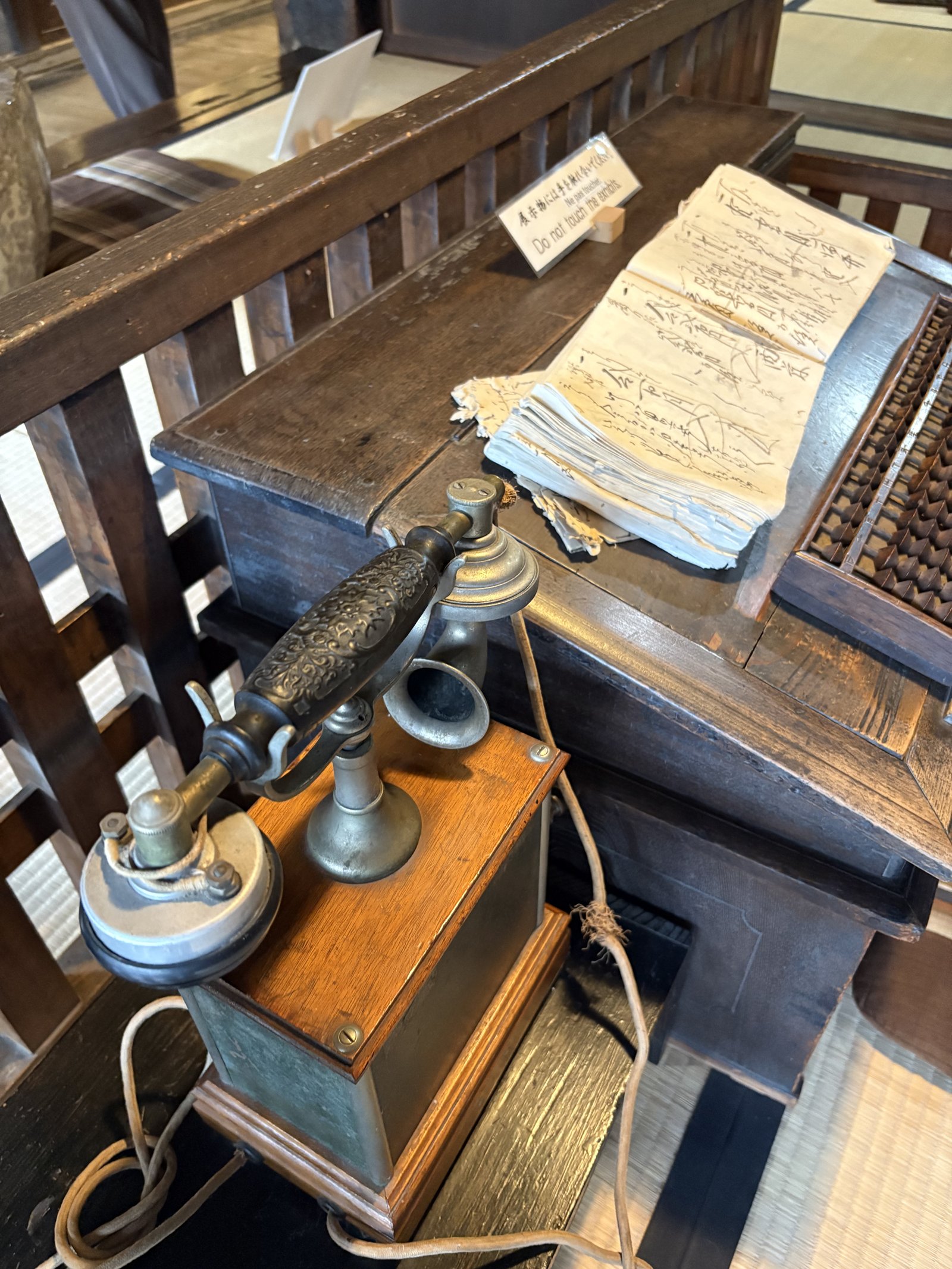An old wall telephone, an abacus and ledgers on a wooden desk