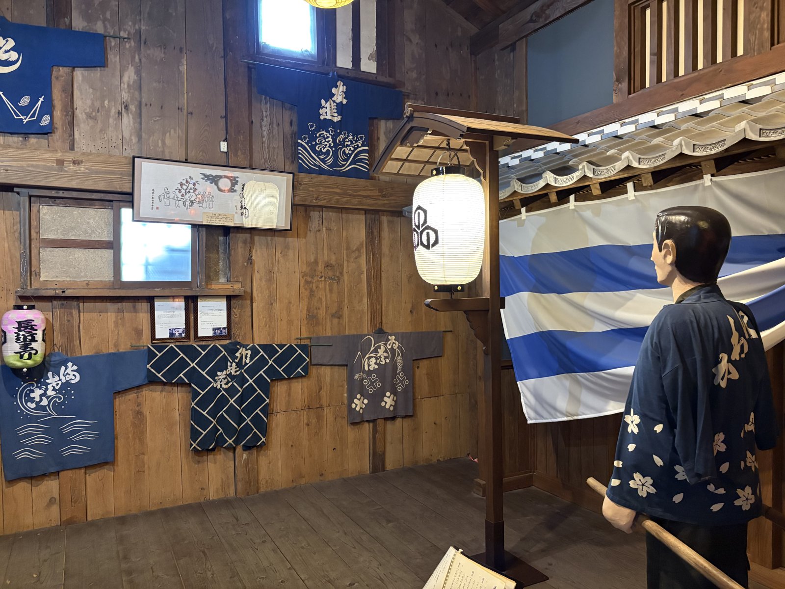 Indigo festival coats hanging on a wooden wall beside a lantern