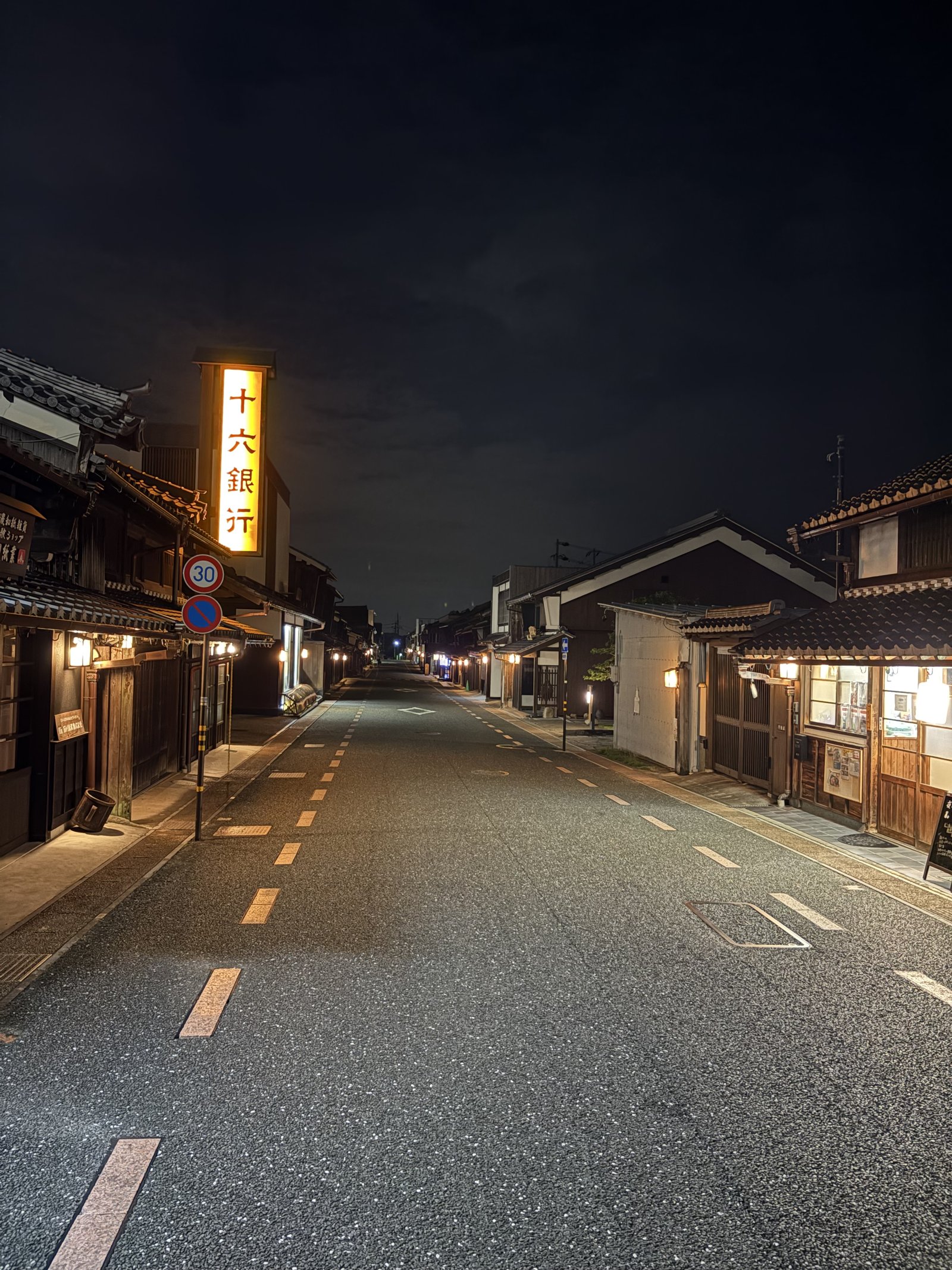A quiet street of old houses at night with a lit bank sign