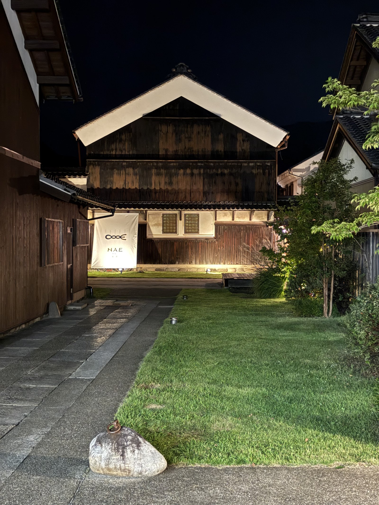 An old storehouse lit up at night at the end of a lawn