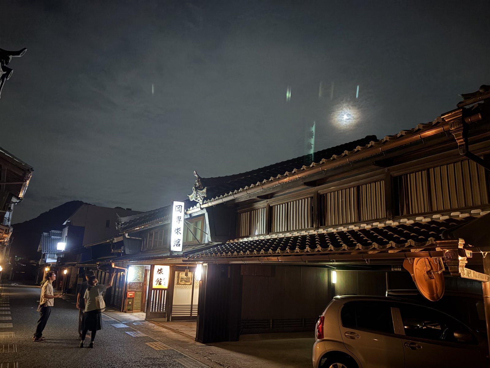 Old wooden merchant houses lit up at night with the moon above the rooftops