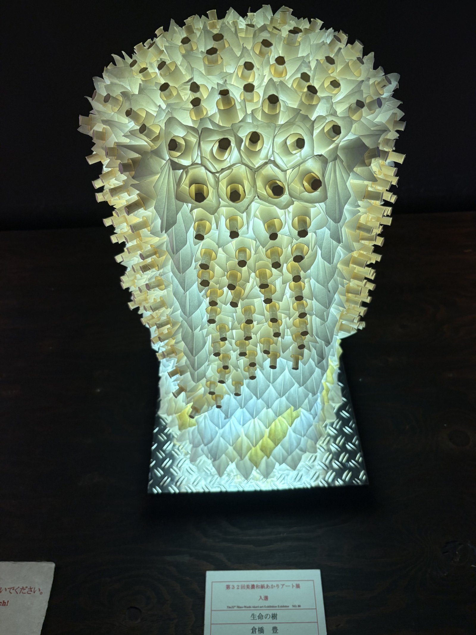 A tall lamp of paper rolled into tubes and spikes, lit green and white