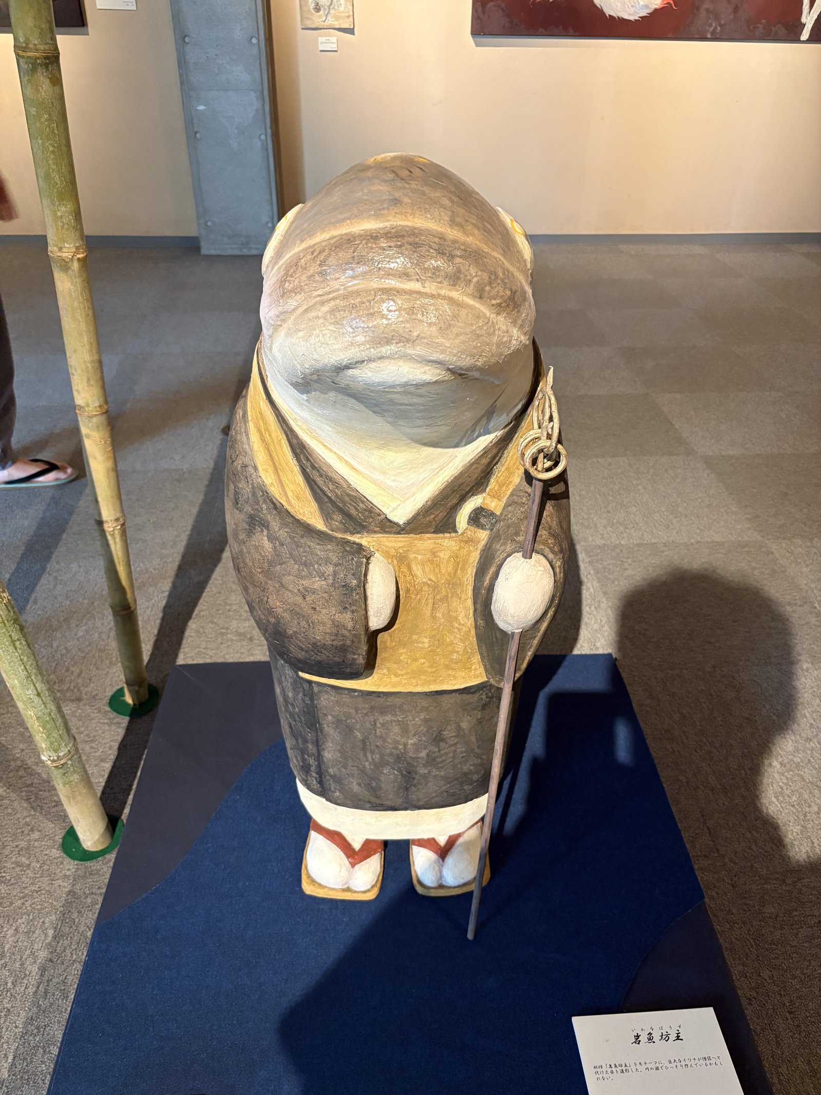 A paper figure in a straw hat and robes holding a staff